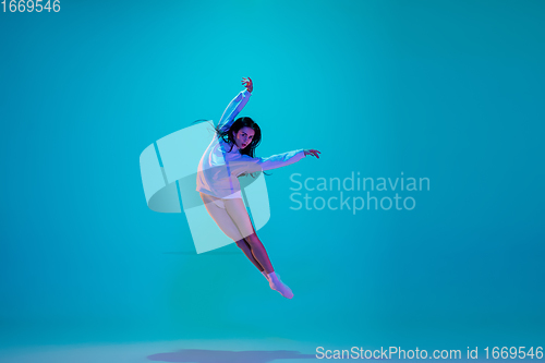 Image of Young and graceful ballet dancer isolated on blue studio background in neon light. Art, motion, action, flexibility, inspiration concept.