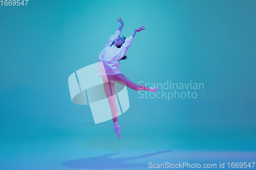 Image of Young and graceful ballet dancer isolated on blue studio background in neon light. Art, motion, action, flexibility, inspiration concept.