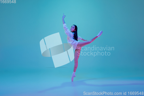 Image of Young and graceful ballet dancer isolated on blue studio background in neon light. Art, motion, action, flexibility, inspiration concept.