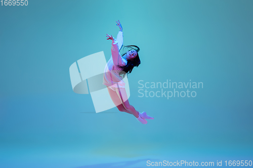 Image of Young and graceful ballet dancer isolated on blue studio background in neon light. Art, motion, action, flexibility, inspiration concept.