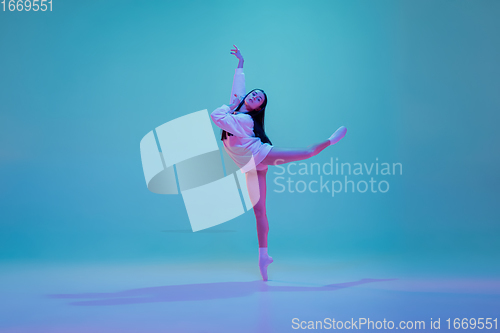 Image of Young and graceful ballet dancer isolated on blue studio background in neon light. Art, motion, action, flexibility, inspiration concept.