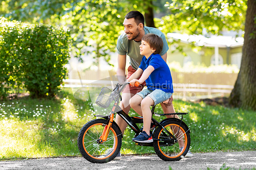 Image of father teaching little son to ride bicycle at park