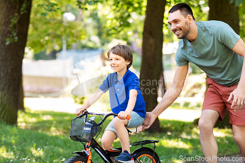 Image of father teaching little son to ride bicycle at park