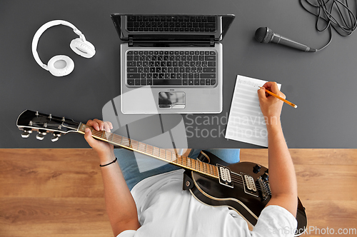 Image of man with guitar writing to music book at table