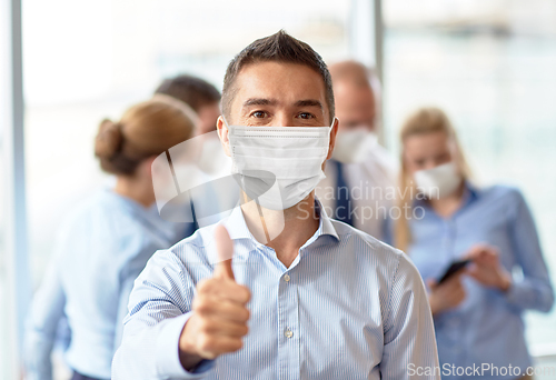 Image of businessman in mask showing thumbs up at office