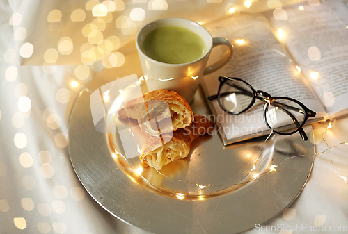 Image of croissants, matcha tea, book and glasses in bed