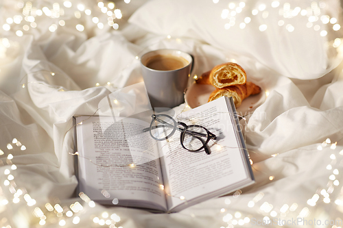 Image of croissants, cup of coffee, book and glasses in bed