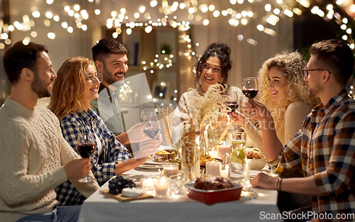 Image of happy friends drinking red wine at christmas party