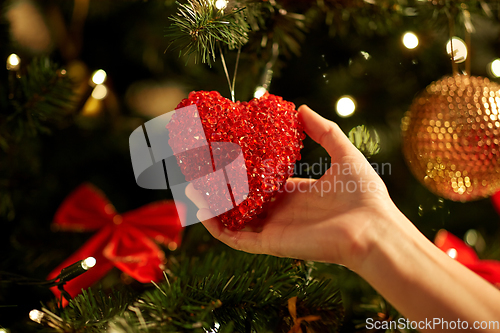 Image of hands decorating christmas tree with red heart