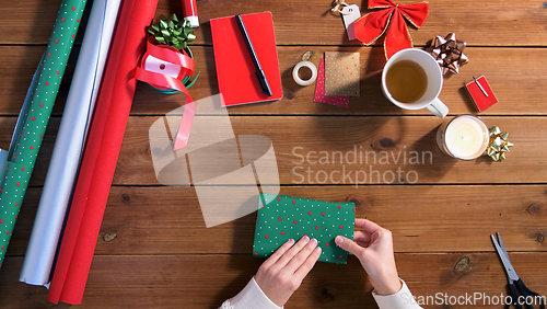 Image of hands wrapping christmas gift into paper at home