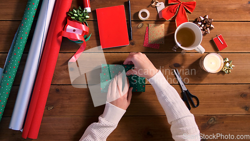 Image of hands wrapping christmas gift into paper at home