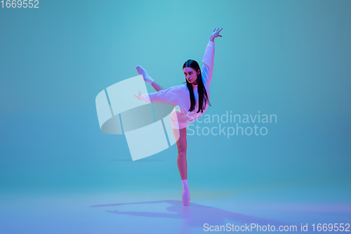Image of Young and graceful ballet dancer isolated on blue studio background in neon light. Art, motion, action, flexibility, inspiration concept.