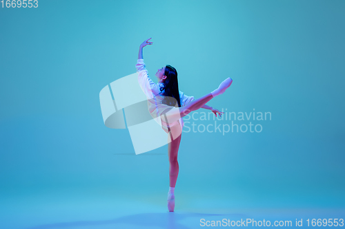 Image of Young and graceful ballet dancer isolated on blue studio background in neon light. Art, motion, action, flexibility, inspiration concept.