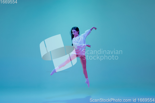 Image of Young and graceful ballet dancer isolated on blue studio background in neon light. Art, motion, action, flexibility, inspiration concept.