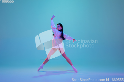 Image of Young and graceful ballet dancer isolated on blue studio background in neon light. Art, motion, action, flexibility, inspiration concept.