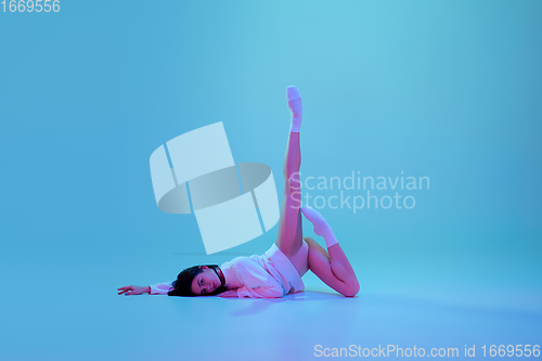 Image of Young and graceful ballet dancer isolated on blue studio background in neon light. Art, motion, action, flexibility, inspiration concept.