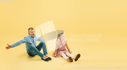 Image of Childhood and dream about big and famous future. Boy and girl isolated on yellow studio background