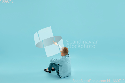 Image of Childhood and dream about big and famous future. Pretty little boy isolated on blue background