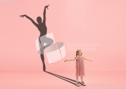 Image of Childhood and dream about big and famous future. Conceptual image with girl and shadow of fit female ballet dancer on coral pink background