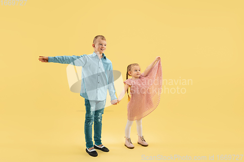 Image of Childhood and dream about big and famous future. Boy and girl isolated on yellow studio background