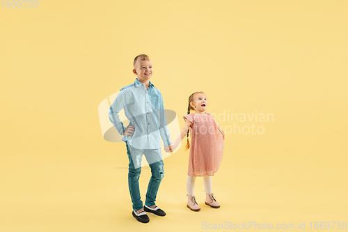 Image of Childhood and dream about big and famous future. Boy and girl isolated on yellow studio background