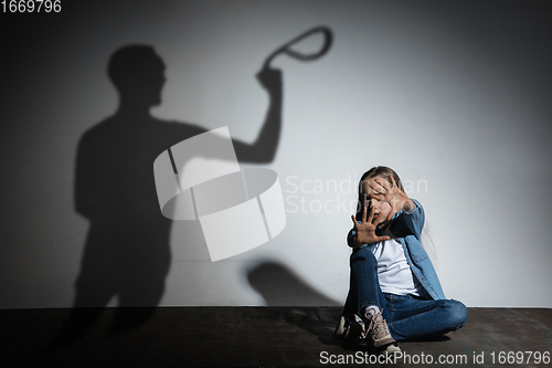 Image of Domestic violence, abusing. Scared little caucasian girl, victim sitting close to white wall with shadow of angry father\'s threatening on it.