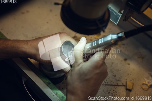 Image of Close up hands of jeweller, goldsmiths making of golden ring with gemstone using professional tools.