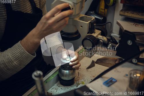 Image of Close up hands of jeweller, goldsmiths making of golden cross with gemstone using professional tools.