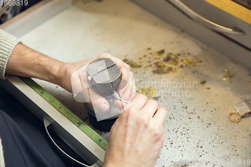 Image of Close up hands of jeweller, goldsmiths making of golden ring with gemstone using professional tools.