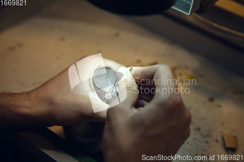 Image of Close up hands of jeweller, goldsmiths making of golden ring with gemstone using professional tools.