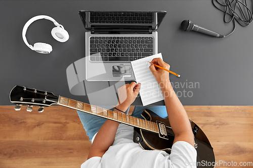 Image of man with guitar writing to music book at table