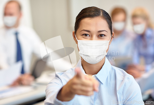 Image of businesswoman in mask pointing finger at office