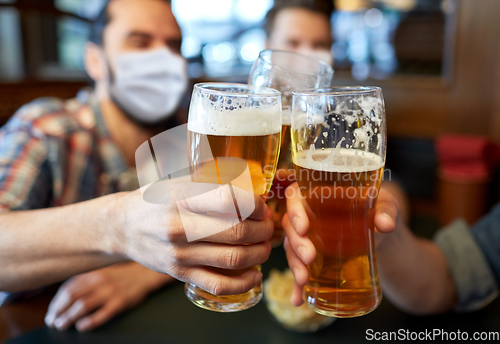 Image of male friends in masks drinking beer at bar or pub