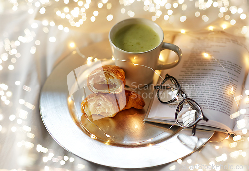 Image of croissants, matcha tea, book and glasses in bed