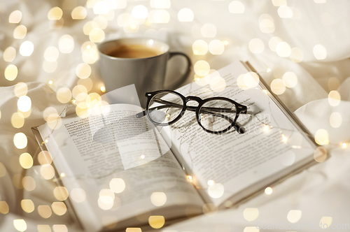 Image of cup of coffee, book, glasses and garland in bed