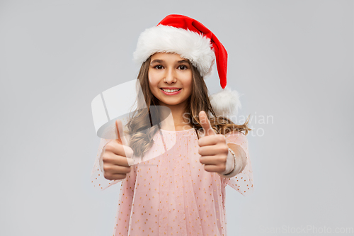 Image of happy teenage girl in santa hat showing thumbs up