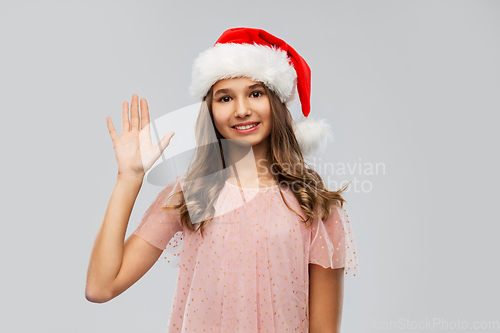 Image of happy teenage girl in santa hat waving hand