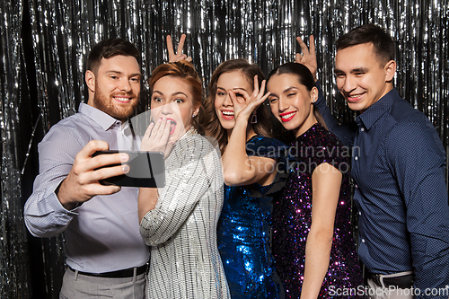 Image of happy friends taking selfie by smartphone at party