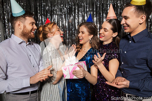 Image of happy friends in party hats with birthday gift