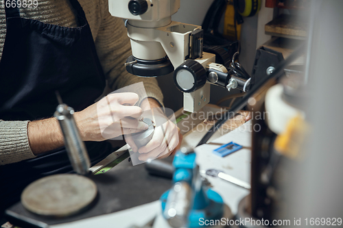 Image of Close up hands of jeweller, goldsmiths making of golden ring with gemstone using professional tools.