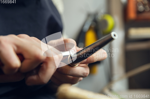 Image of Close up hands of jeweller, goldsmiths making of golden ring with gemstone using professional tools.