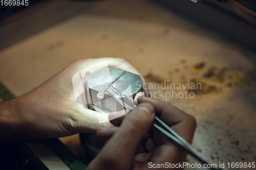 Image of Close up hands of jeweller, goldsmiths making of golden ring with gemstone using professional tools.
