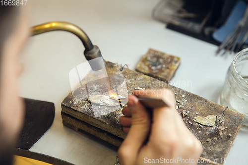 Image of Close up hands of jeweller, goldsmiths making of golden ring with gemstone using professional tools.