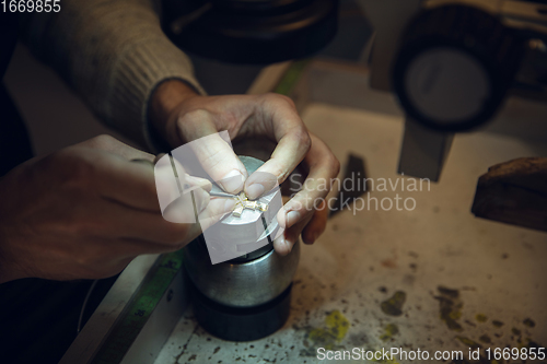 Image of Close up hands of jeweller, goldsmiths making of golden cross with gemstone using professional tools.