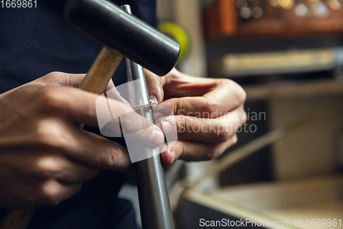 Image of Close up hands of jeweller, goldsmiths making of golden ring with gemstone using professional tools.