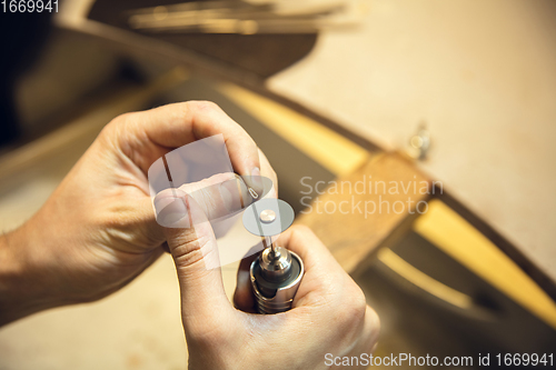 Image of Close up hands of jeweller, goldsmiths making of silver ring with gemstone using professional tools.