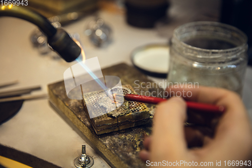 Image of Close up hands of jeweller, goldsmiths making of silver ring with gemstone using professional tools.