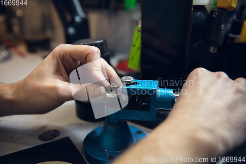 Image of Close up hands of jeweller, goldsmiths making of silver ring with gemstone using professional tools.