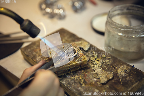 Image of Close up hands of jeweller, goldsmiths making of silver ring with gemstone using professional tools.