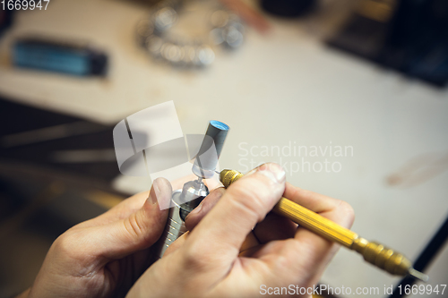 Image of Close up hands of jeweller, goldsmiths making of silver ring with gemstone using professional tools.